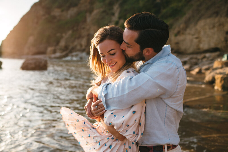 Couple embrace at sunset, the breeze catches the girls dress at Saunton Sands beach in Devon 
