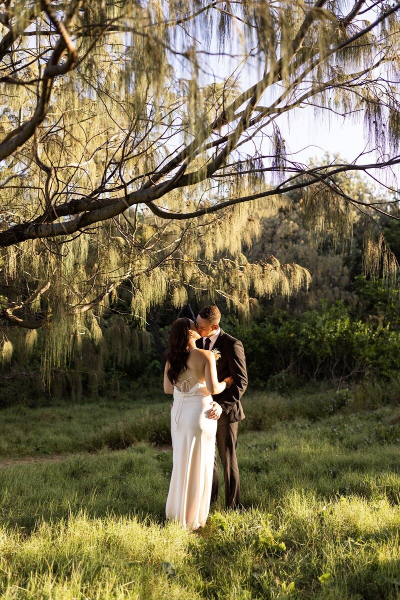 A bride and a groom kissing under a tree