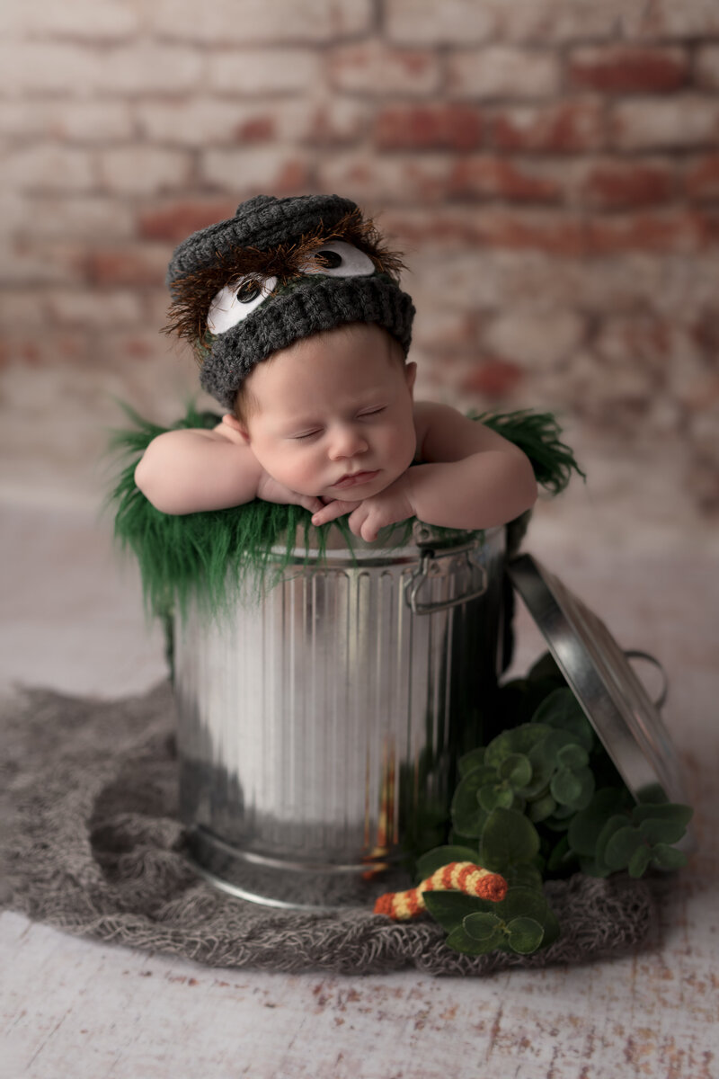 Whimsical Oscar the Grouch newborn session with a metal trash can prop and themed hand-knit hat.