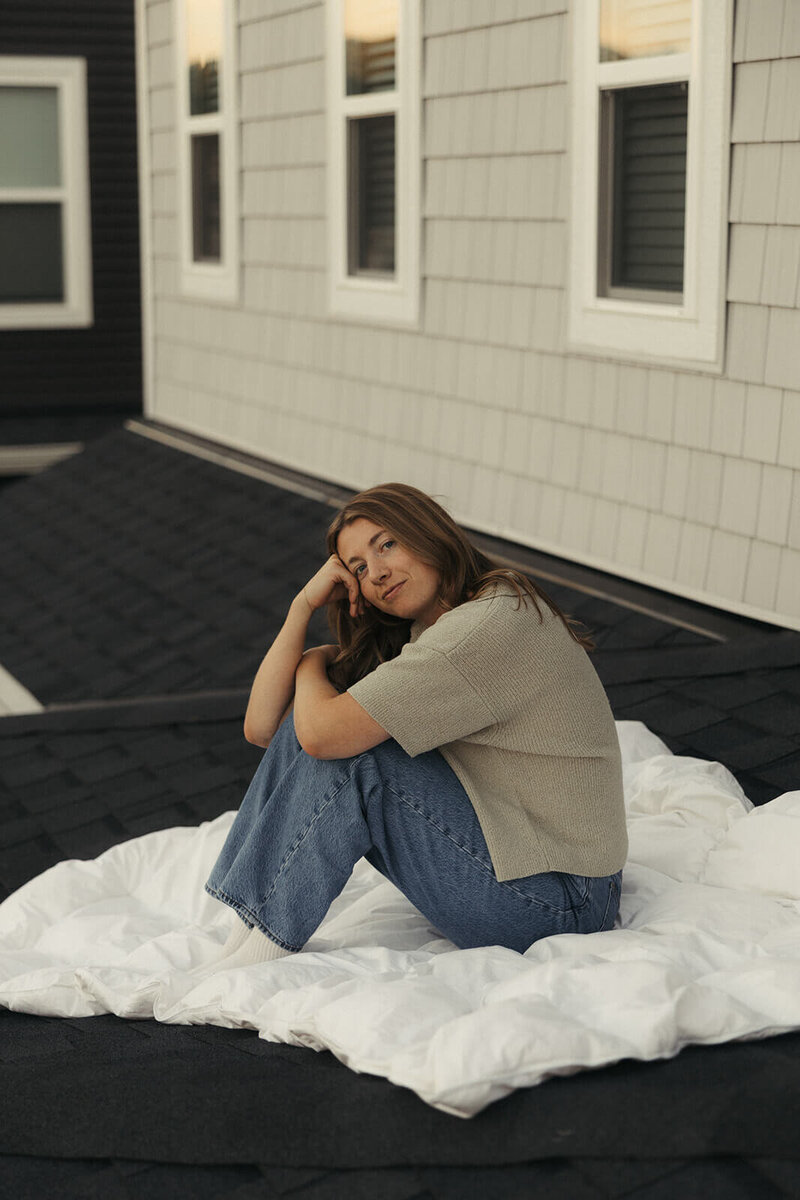 Wedding photographer located in Minnesota sits on white duvet on the rooftop of her home