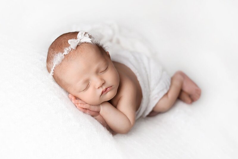 Newborn girl in pure white in side laying beanbag pose at Langley baby photo shoot