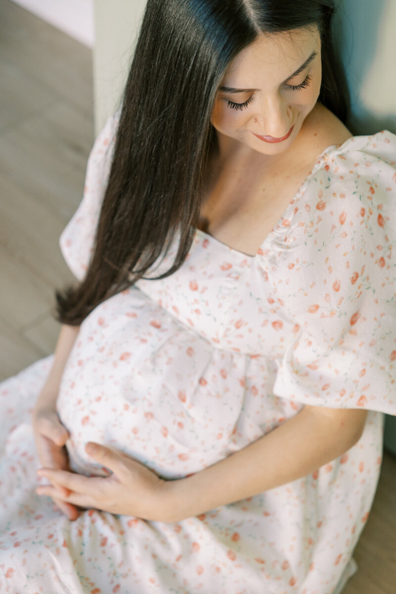 Pregnant woman in flowing white dress holding her baby bump during Fresno maternity photo session