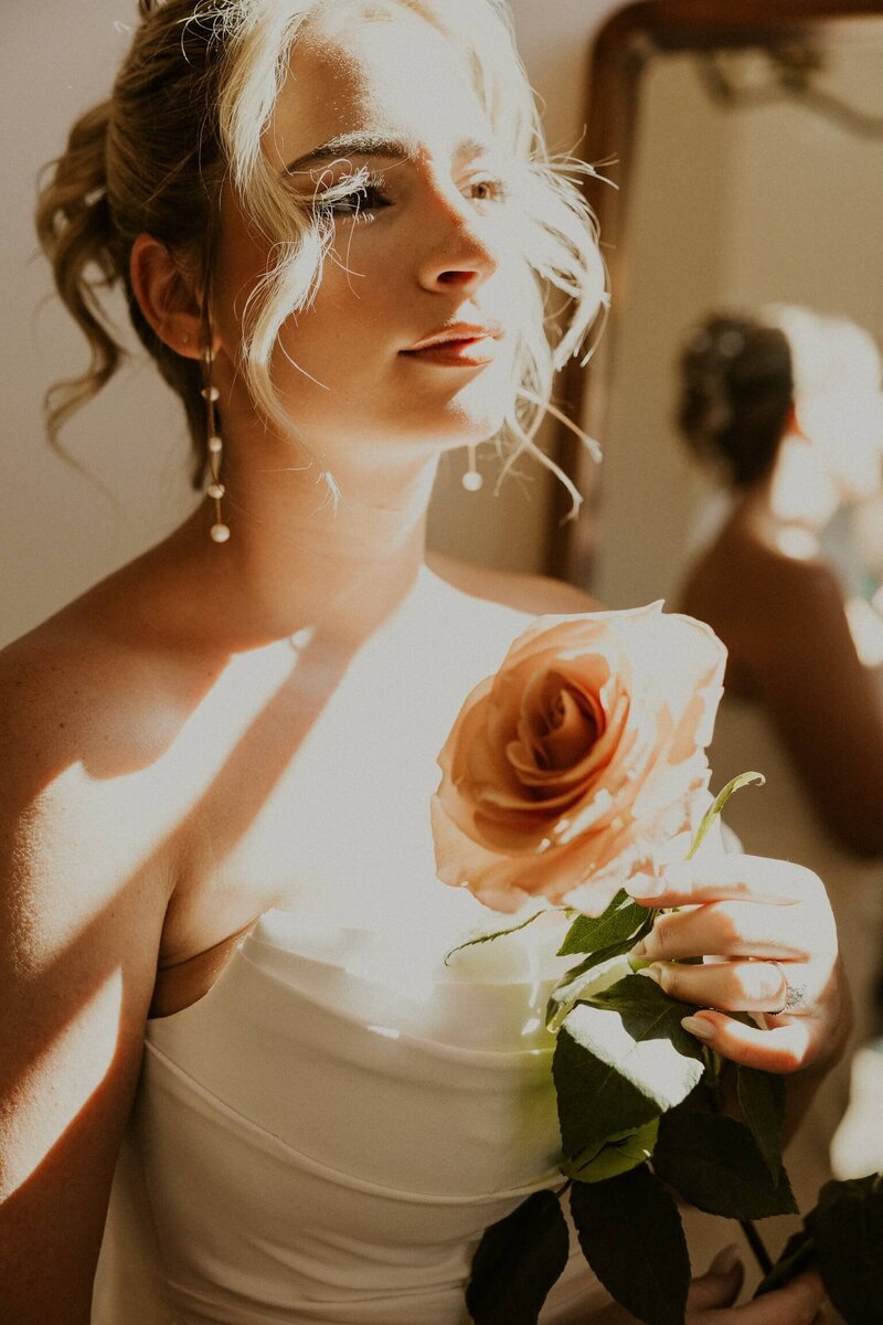 Blonde bride wearing white wedding dress looking down and smiling in playful pose