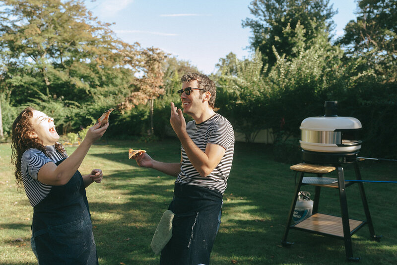 couple laughing with pizza during at home engagement photos, captured by Elsie Goodman, an NYC engagement and couples photographer