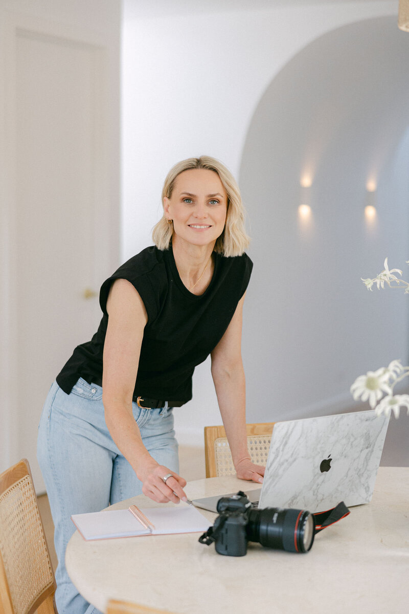 Zelda Green, entrepreneur and money and mindset educator, smiling at camera while working on her laptop on her business resources in her beautiful home