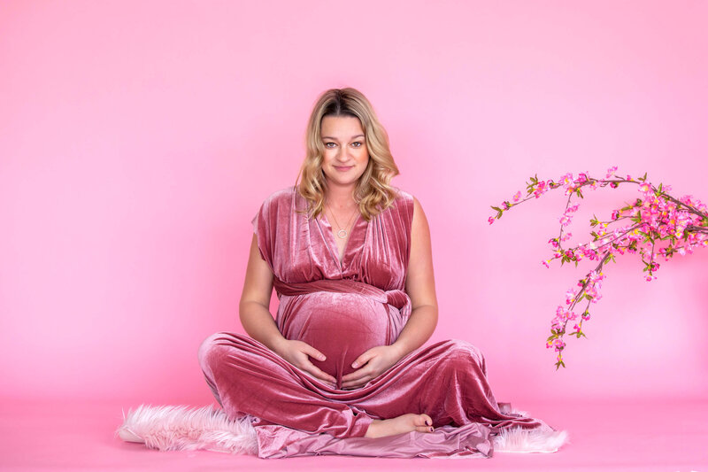 expectant mom in pink velvet dress with pink background and flowers
