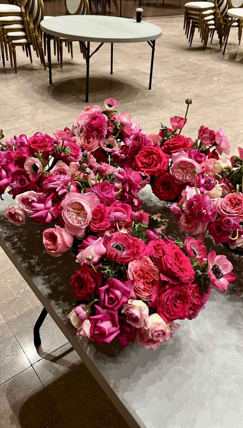 Bright pink wedding centerpiece flowers with roses and ranunculus arranged by a Montreal wedding florist, featuring lush floral centerpieces for wedding tables during event setup.