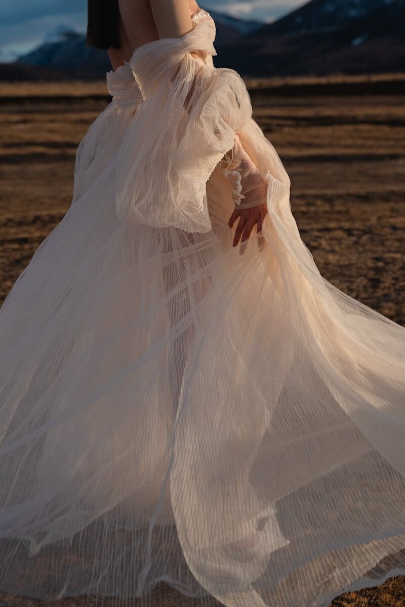 Couture dress bridal shoot on a field with mountains in the background and golden light.
