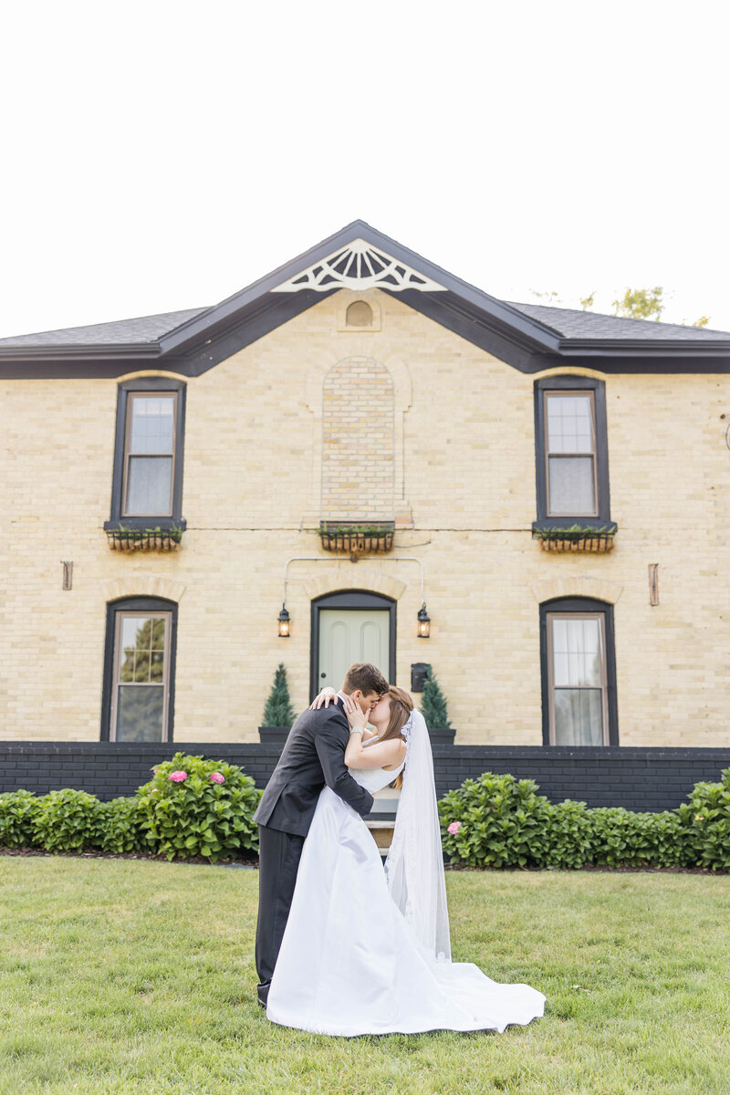 Bride and groom dip kiss in front of their venue Bowery Barn in Wisconsin