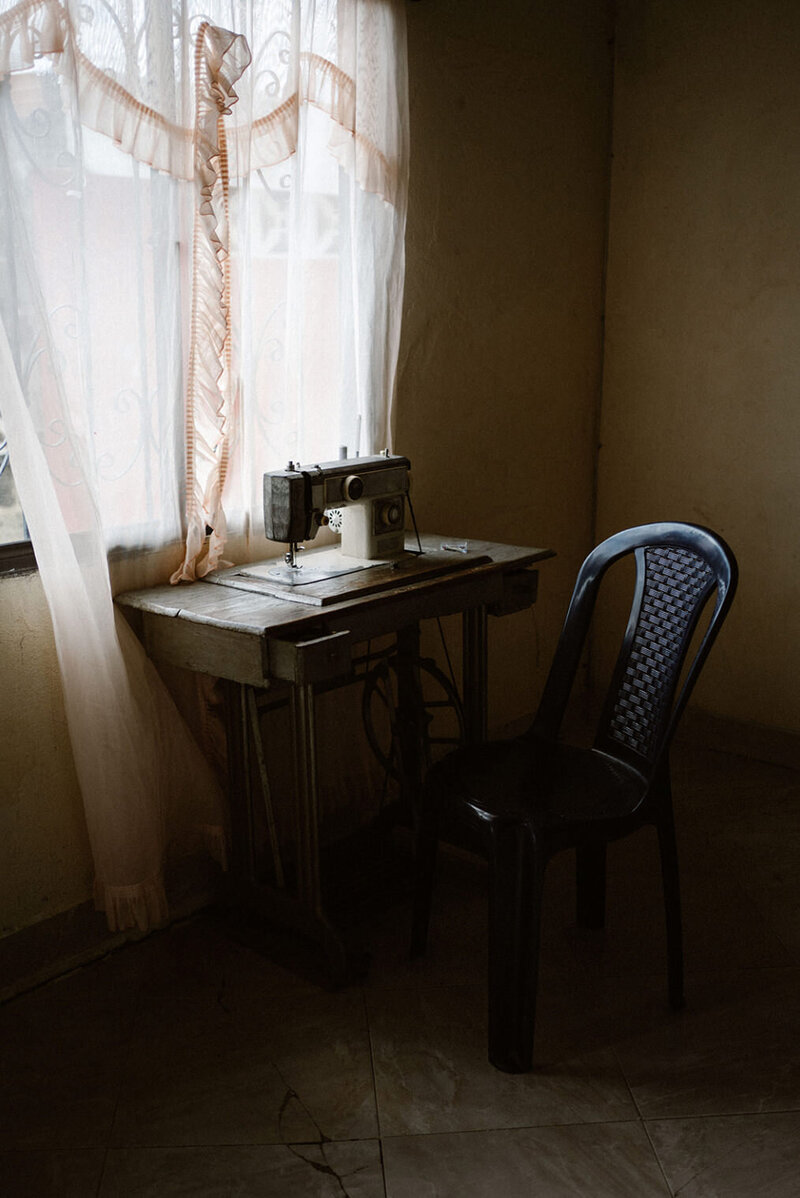 Een naaimachine en plastic stoel naast het gordijn bij het raam
