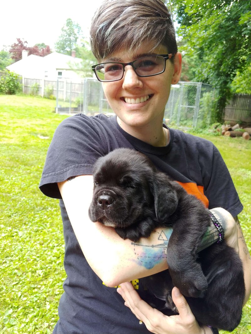 Woman with short hair smiles at camera holding a Cane Corso puppy.