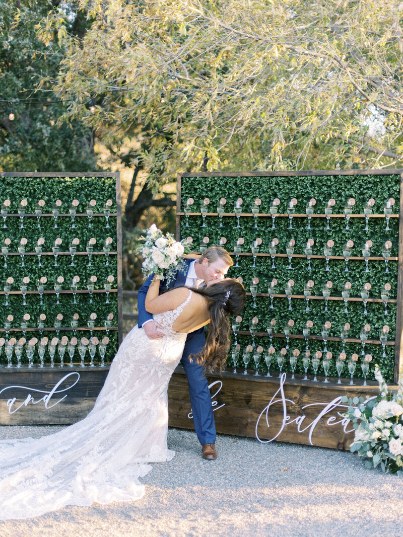 Bride and groom kiss in front of gorgeous escort wall for wedding guests