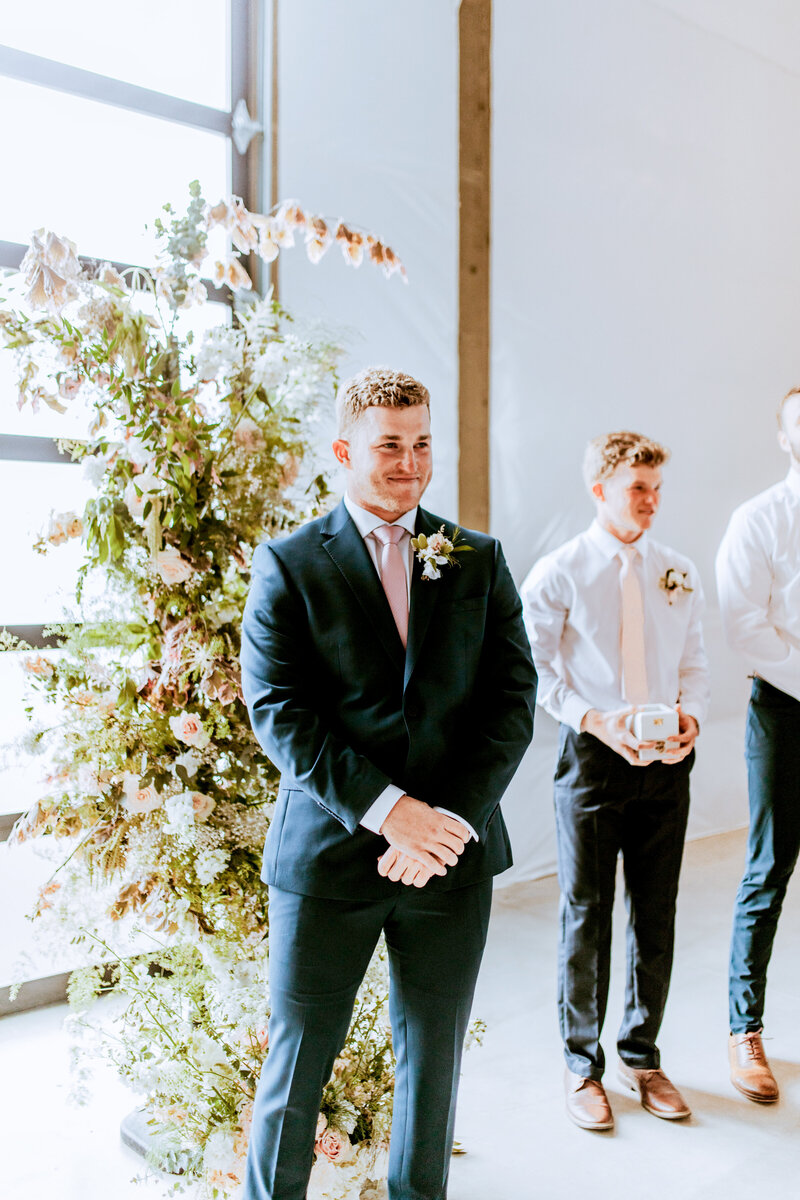 A Groom waits at the altar for his bride, groomsmen in the back.