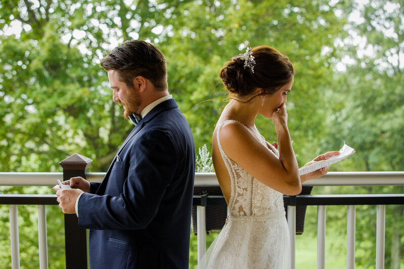 Bride and groom standing back-to-back, crying as they read heartfelt love notes during their first look.