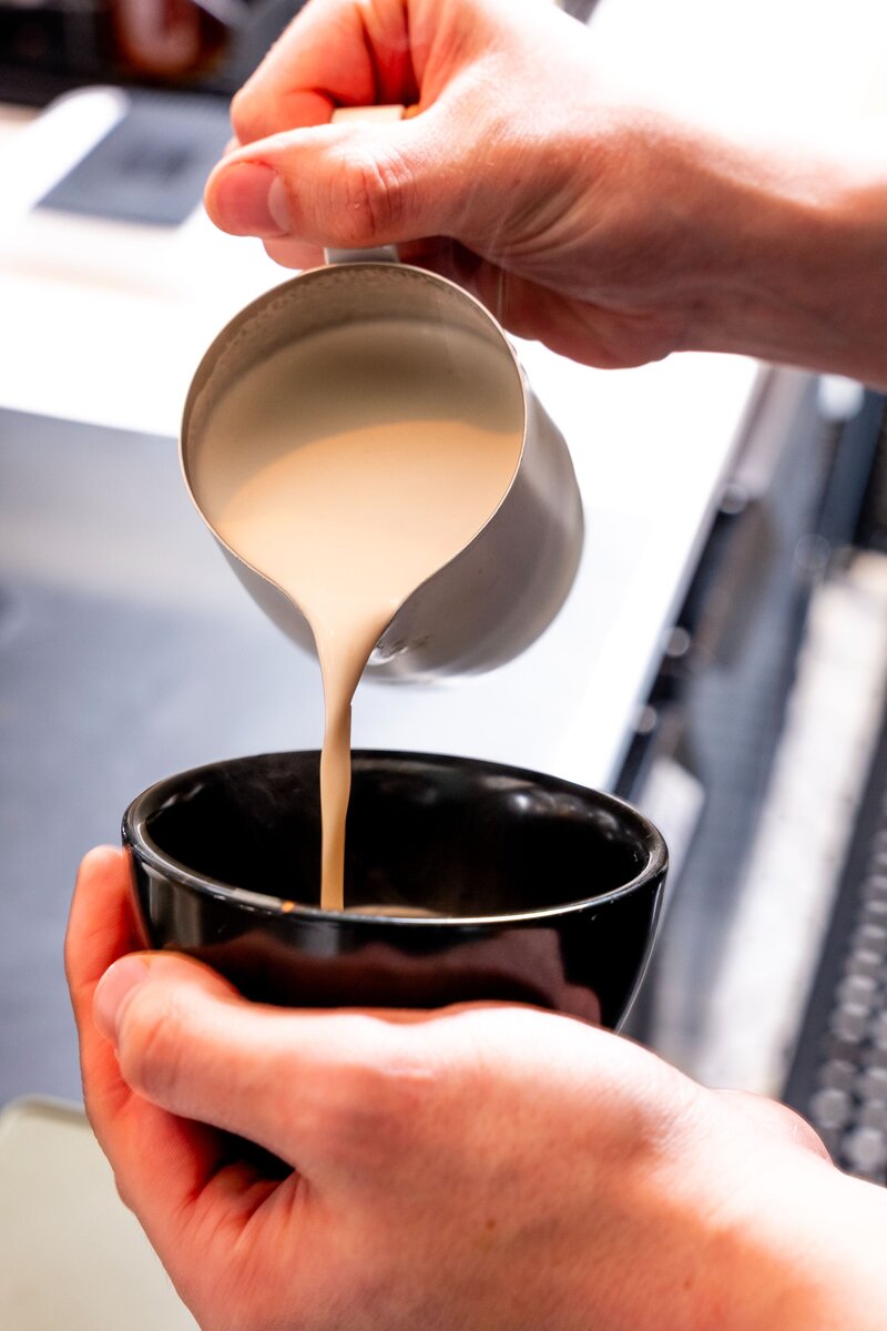 Barista pouring steamed milk into a cup for latte art at Grain Artisan Bakery in Snohomish, WA — showcasing care and precision in every drink.
