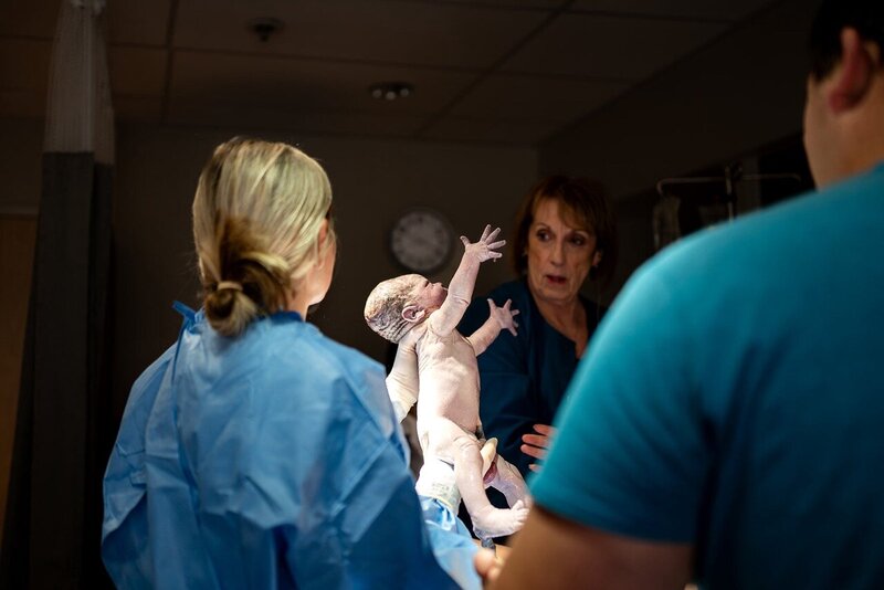 Freshly born baby being held up to meet mother for the first time during a birth session