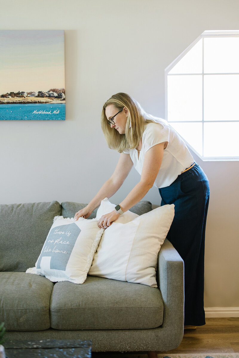 Kim Kussman, Utah Realtor & Owner of Nurture Lane, fluffing pillows in a living room of a utah property listing.