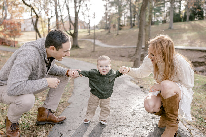 Mother and father holding each of their son's hands while he stands