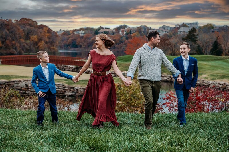 Family walking through grass, holding hands, sunset in the background.