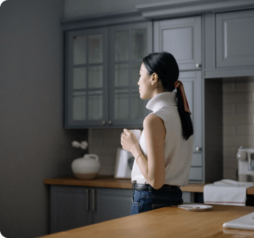 A woman standing in her kitchen holding a white mug.