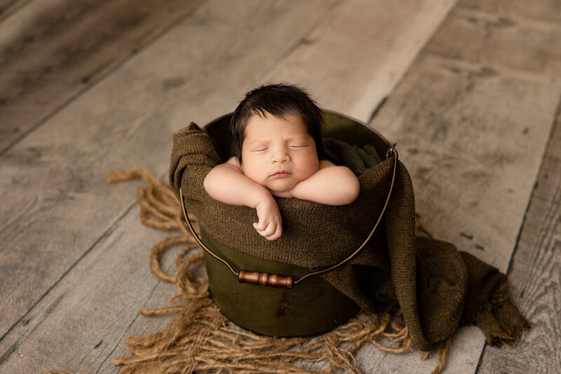 Newborn baby boy in a blue swaddle in a tan basket on a tan background