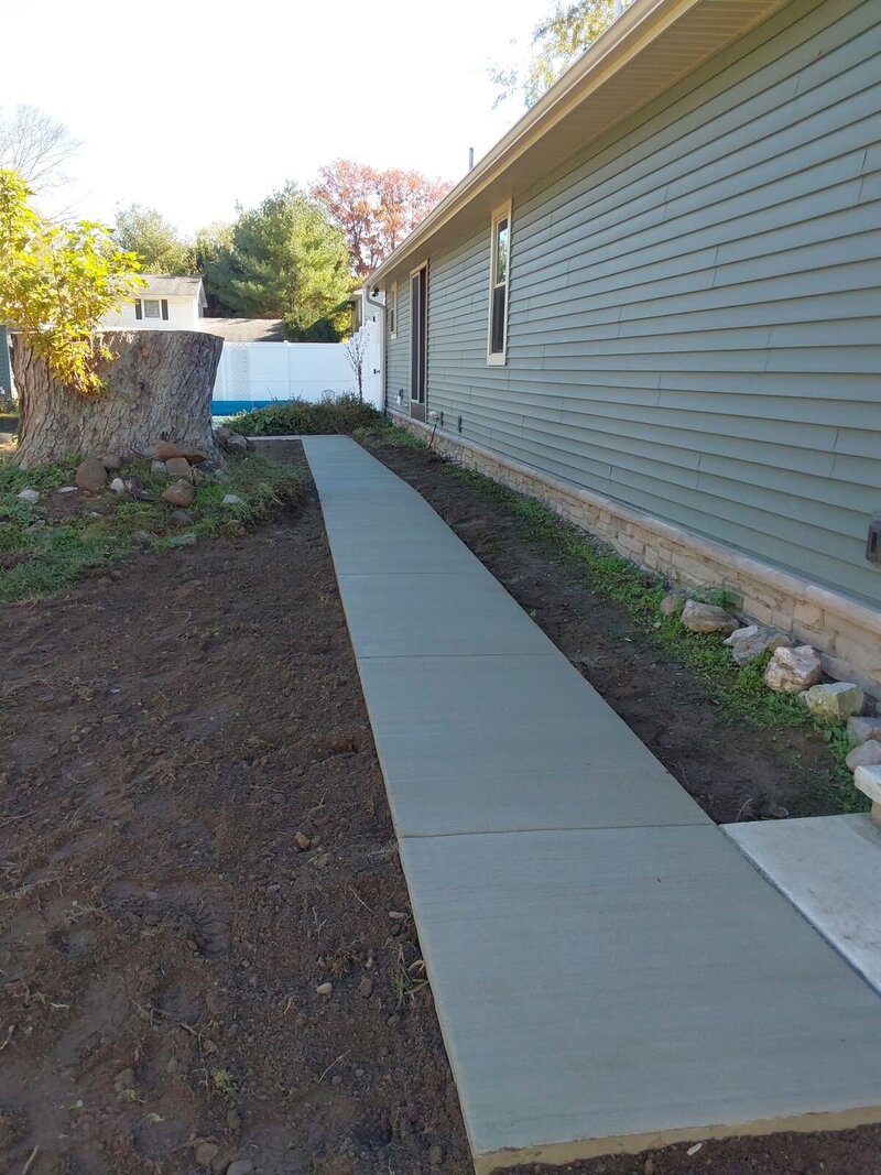 New broom-finish concrete walkway running along the side of a home with green siding and a stone wainscot in Osceola, IN