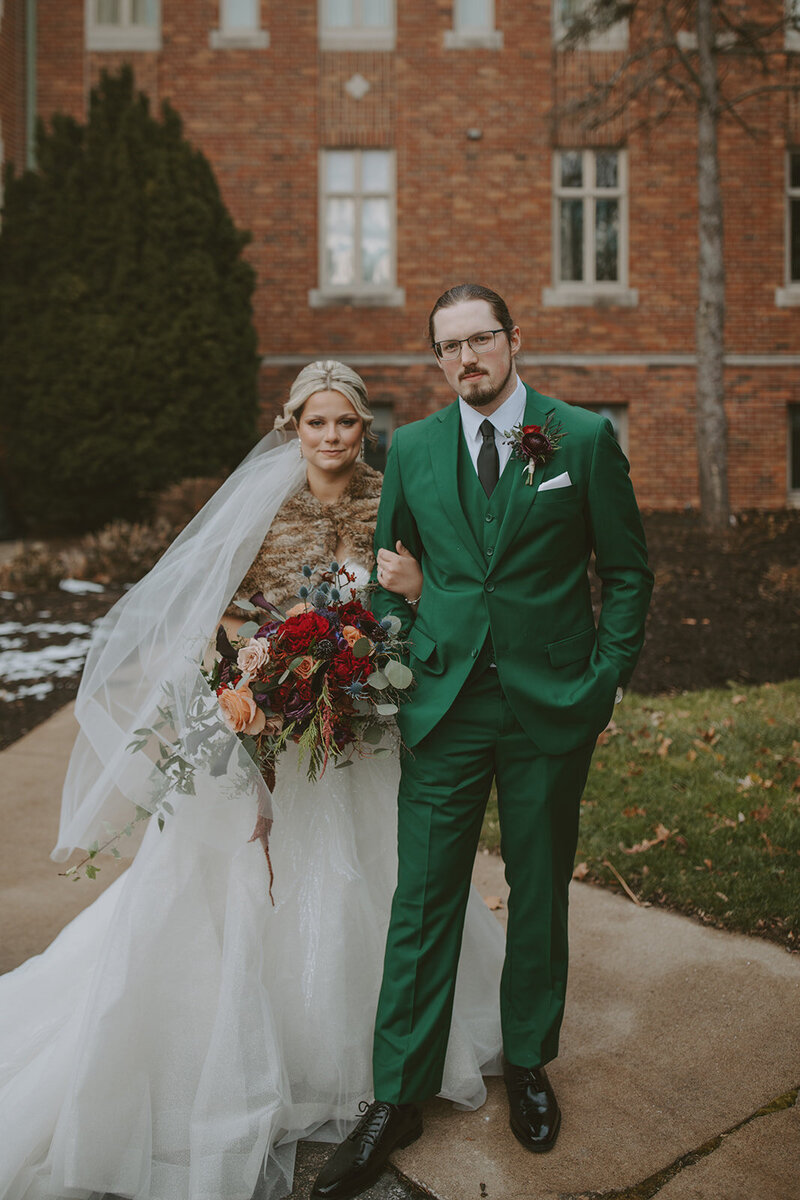 bride and groom pose on a bench in front of rose bush