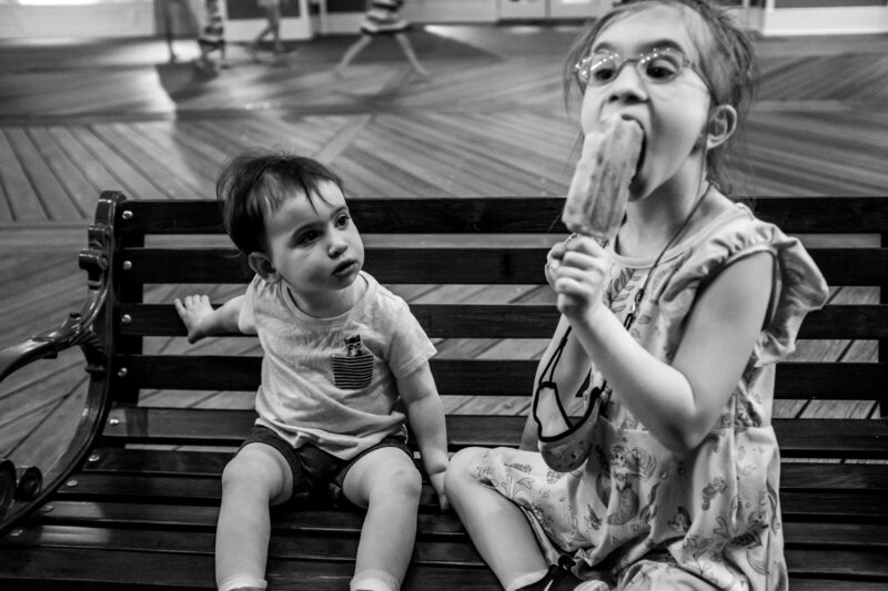 Two children sitting on a bench eating ice cream.