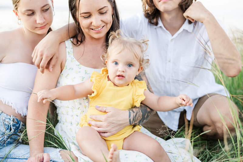 Beautiful family portrait of four with mum, brother and and sister looking at beautiful toddler sister as she looks at the camera. Located on top of a Cooee Bay, Yeppoon hill.