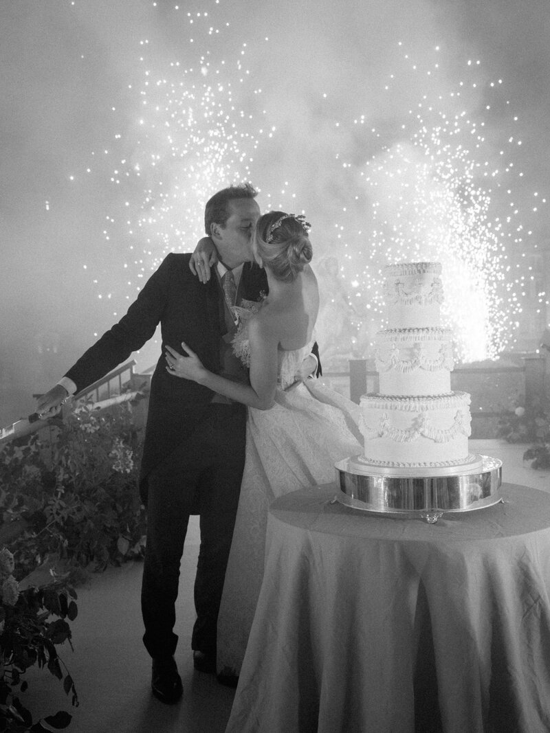 Groom kissing bride in front of wedding cake with fireworks