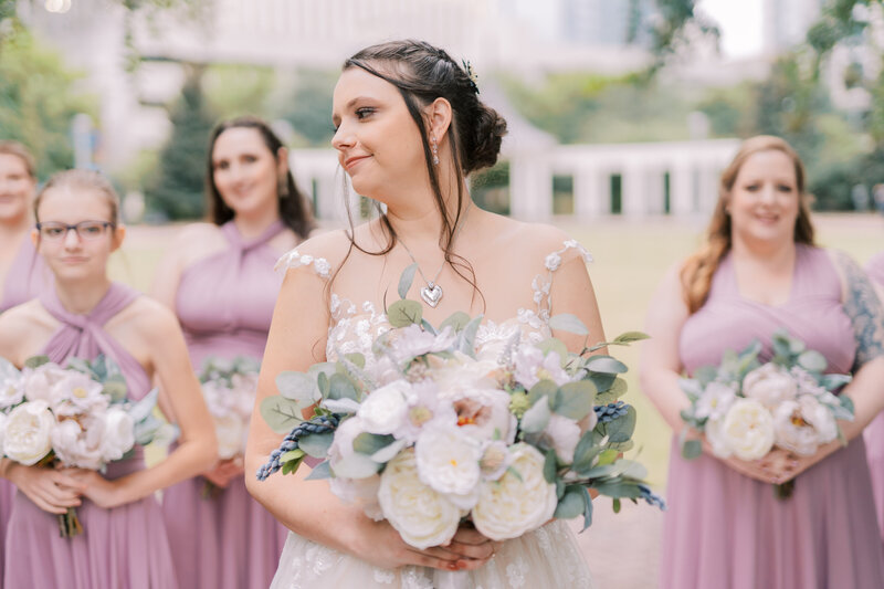 a bride with her bridesmaids and bouquet walking through a garden