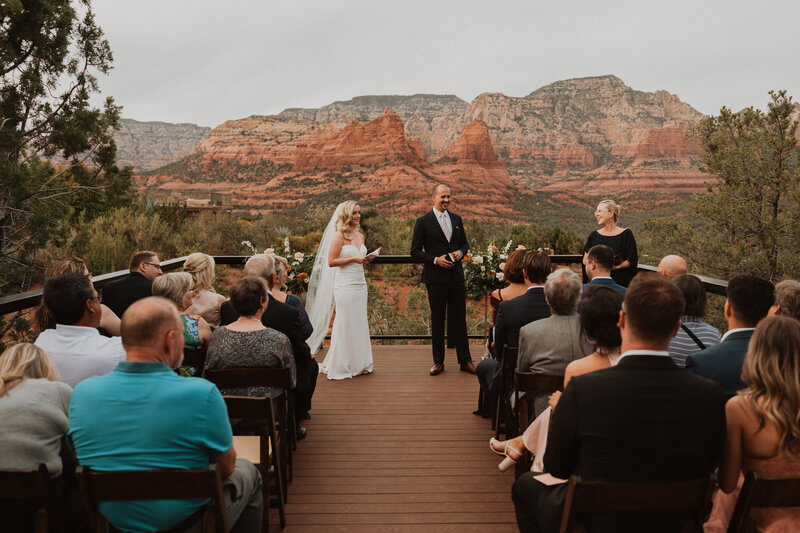 A bride and groom hugging and smiling at an overlook looking out on red rocks.