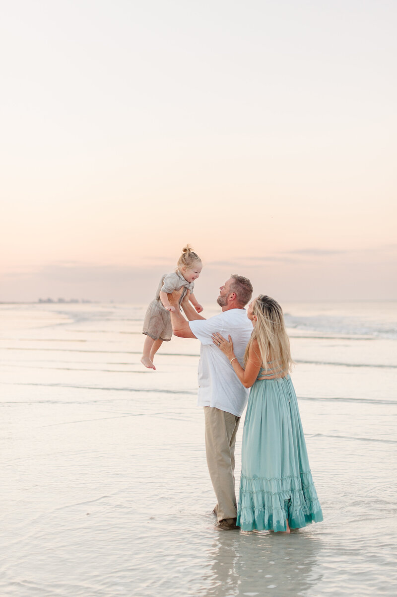 Dad holding son in the air near the beach at sunset during family portraits captured by Orlando photographer