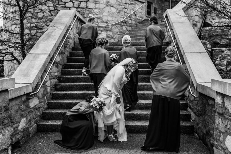 Black and white photo of bride getting train of dress fixed on steps