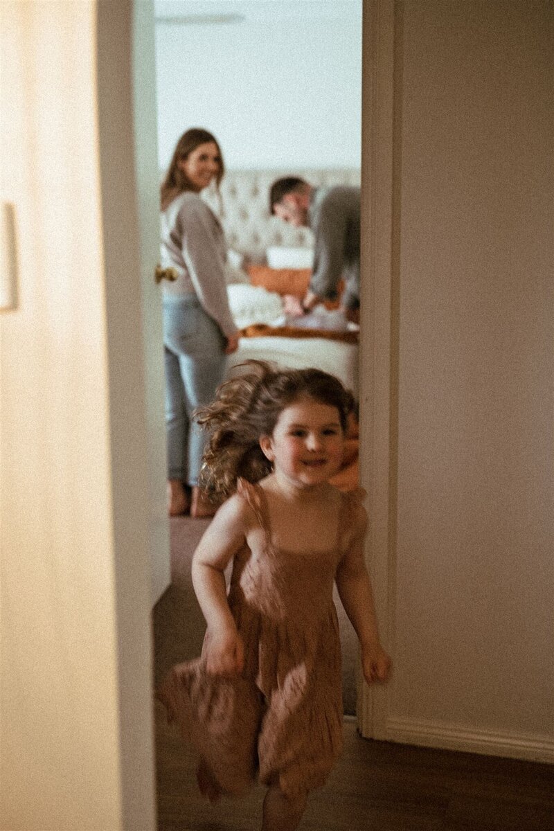 A joyful child runs through a hallway with parents smiling in the background, symbolizing the importance of work-life balance and family time emphasized by KP Virtual Assistance’s mission. Photo credit: Louise Agnew Photography