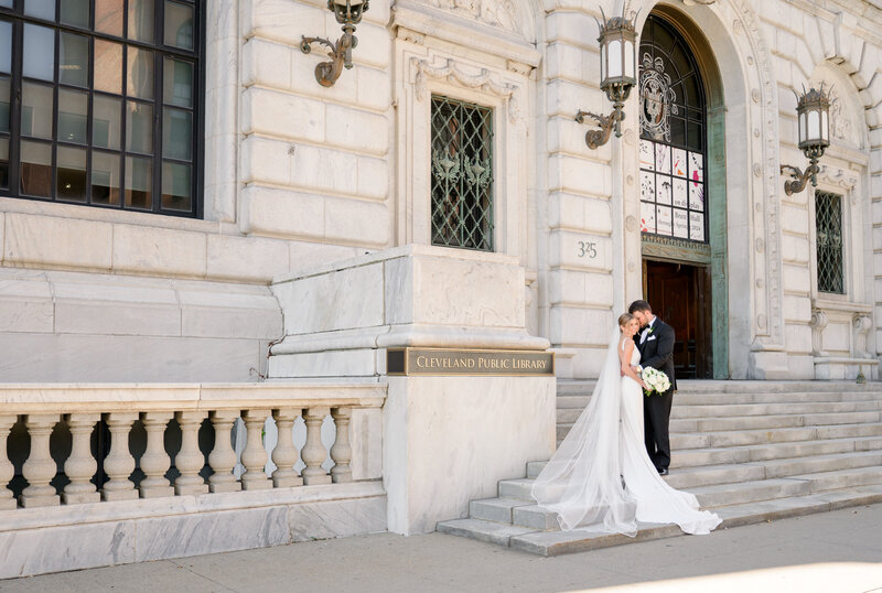 A wide photo of the bride leaning on the grooms shoulder on the stairs of the Old Courthouse in Cleveland