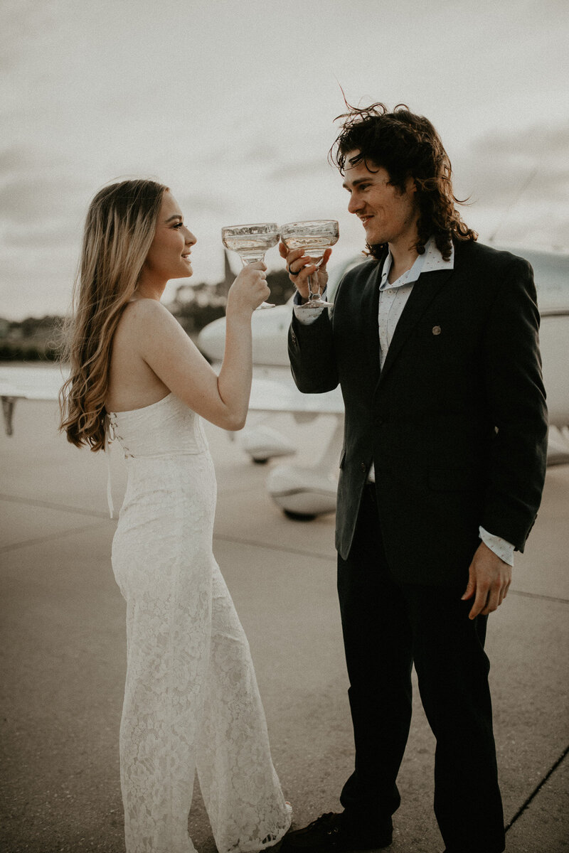 Engaged couple toasting to getting engaged with a plane behind them in Jacksonville, Florida