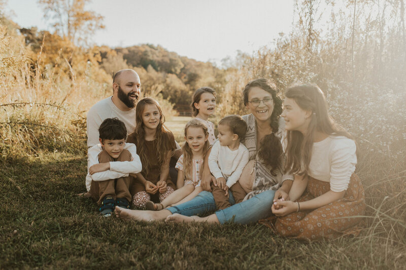 A family with 6 kids sitting down laughing with the mom prgenant with the 7th baby during maternity session in Alcoa Tn