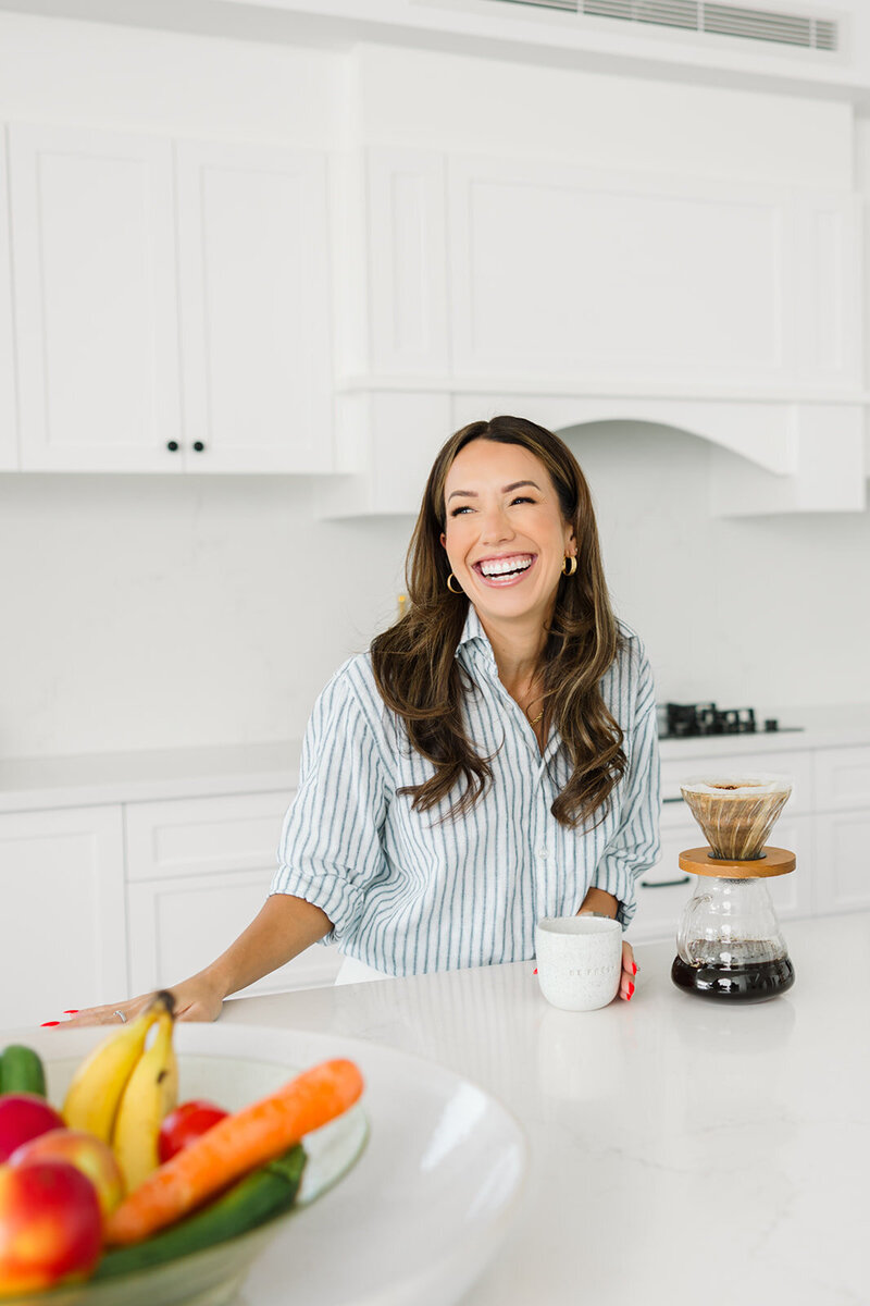 A personal brand, business, and leadership mentor enjoying coffee in a modern white kitchen during a personal branding photoshoot