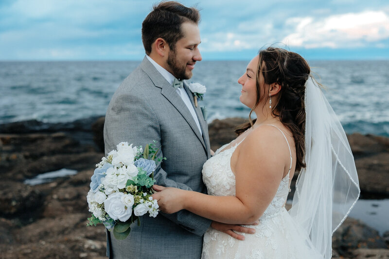 bride and groom standing on black rocks with lake superior in the background
