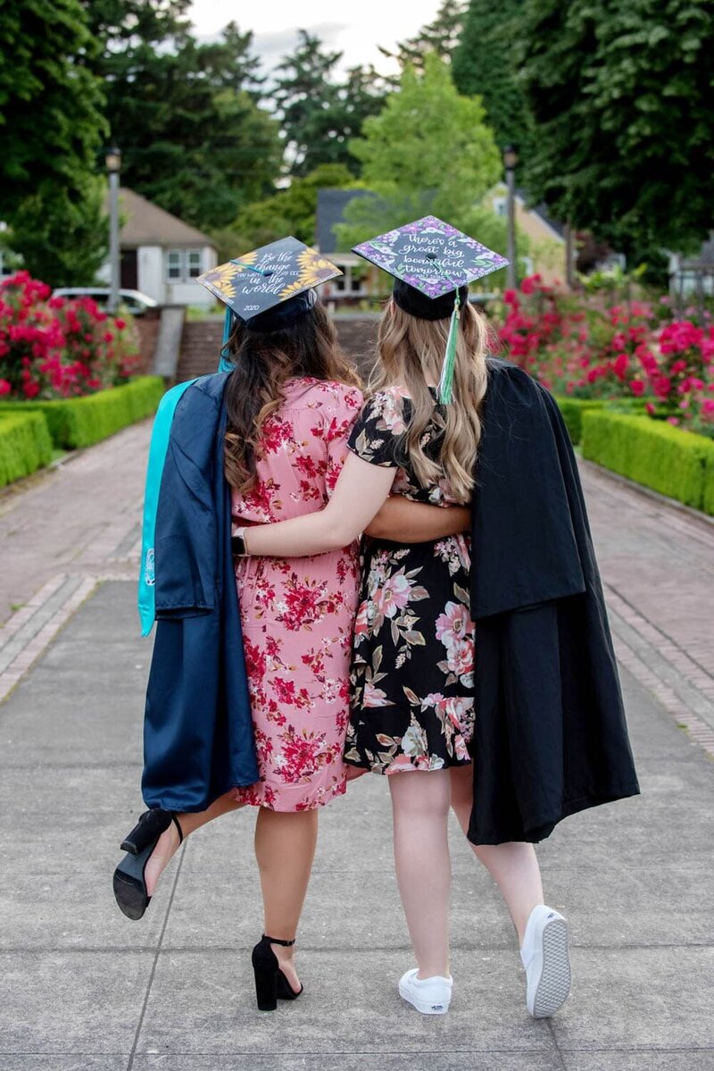 Two best friends wearing colorful dresses with their graduation caps and gowns, with their backs faced towards the camera.
