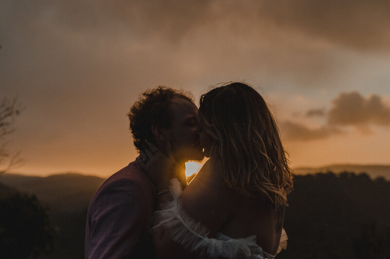 newly married couple kiss at sunset on top of mountain at their elopement