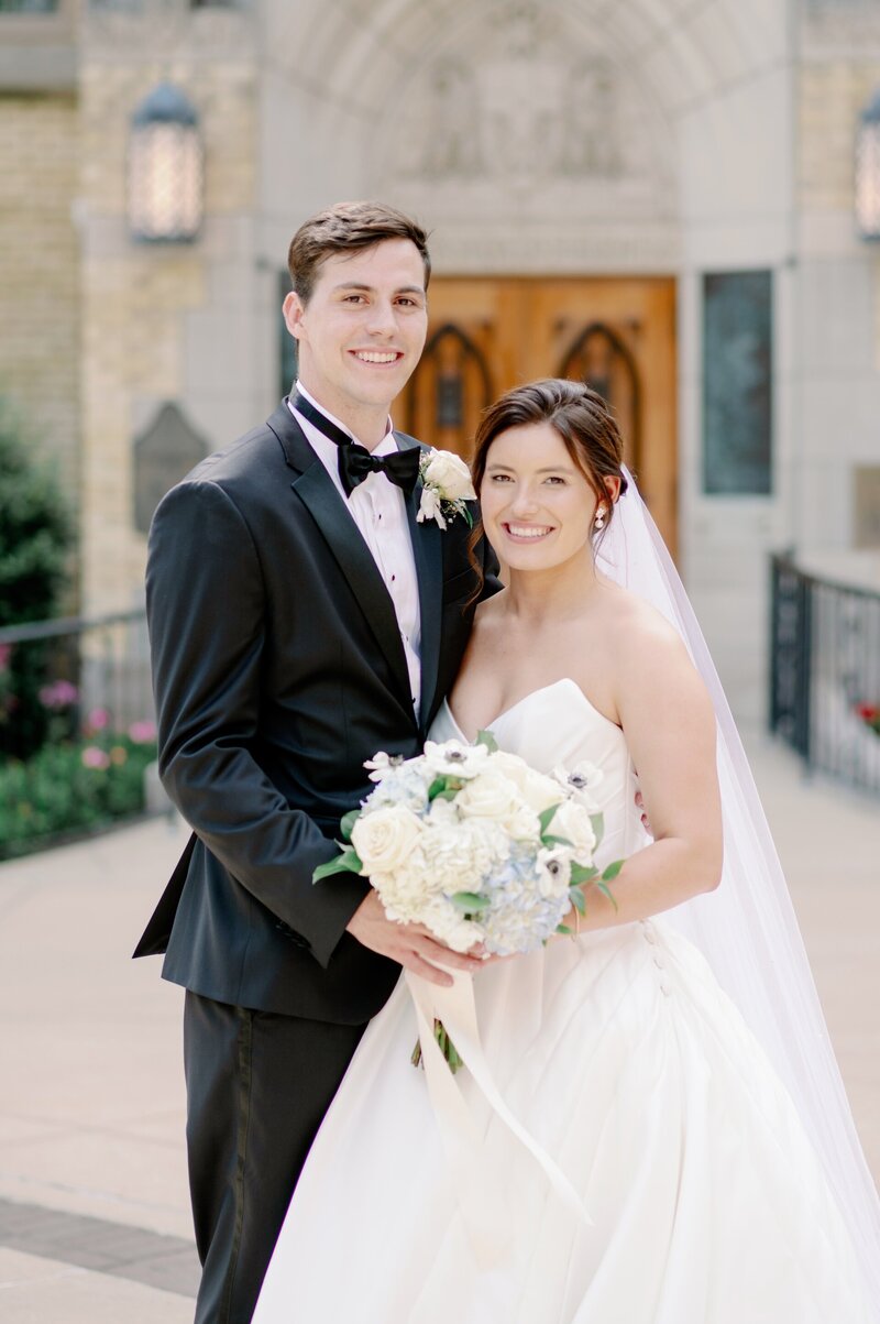 bride and groom smiling in front of a Catholic church at Notre Dame on their wedding day