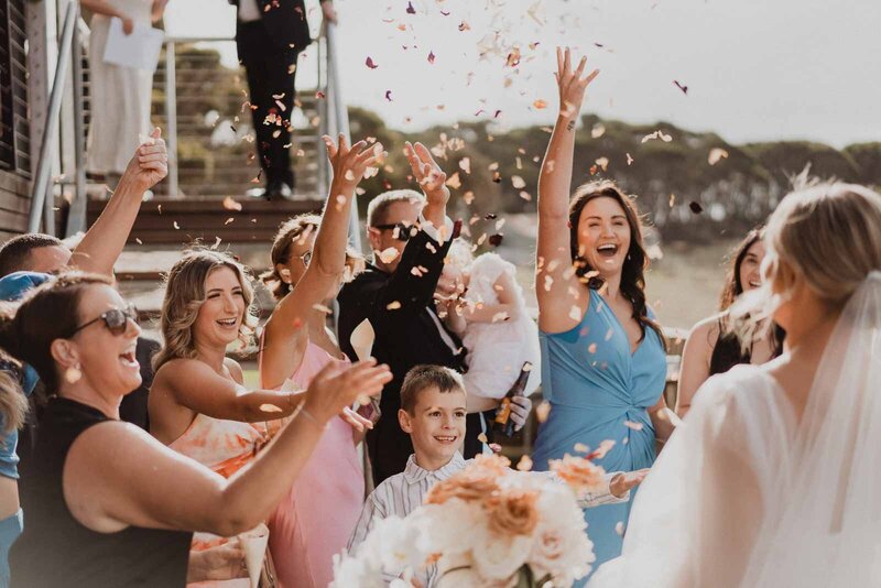 Guest throwing flower petals as bride and groom walk down the aisle