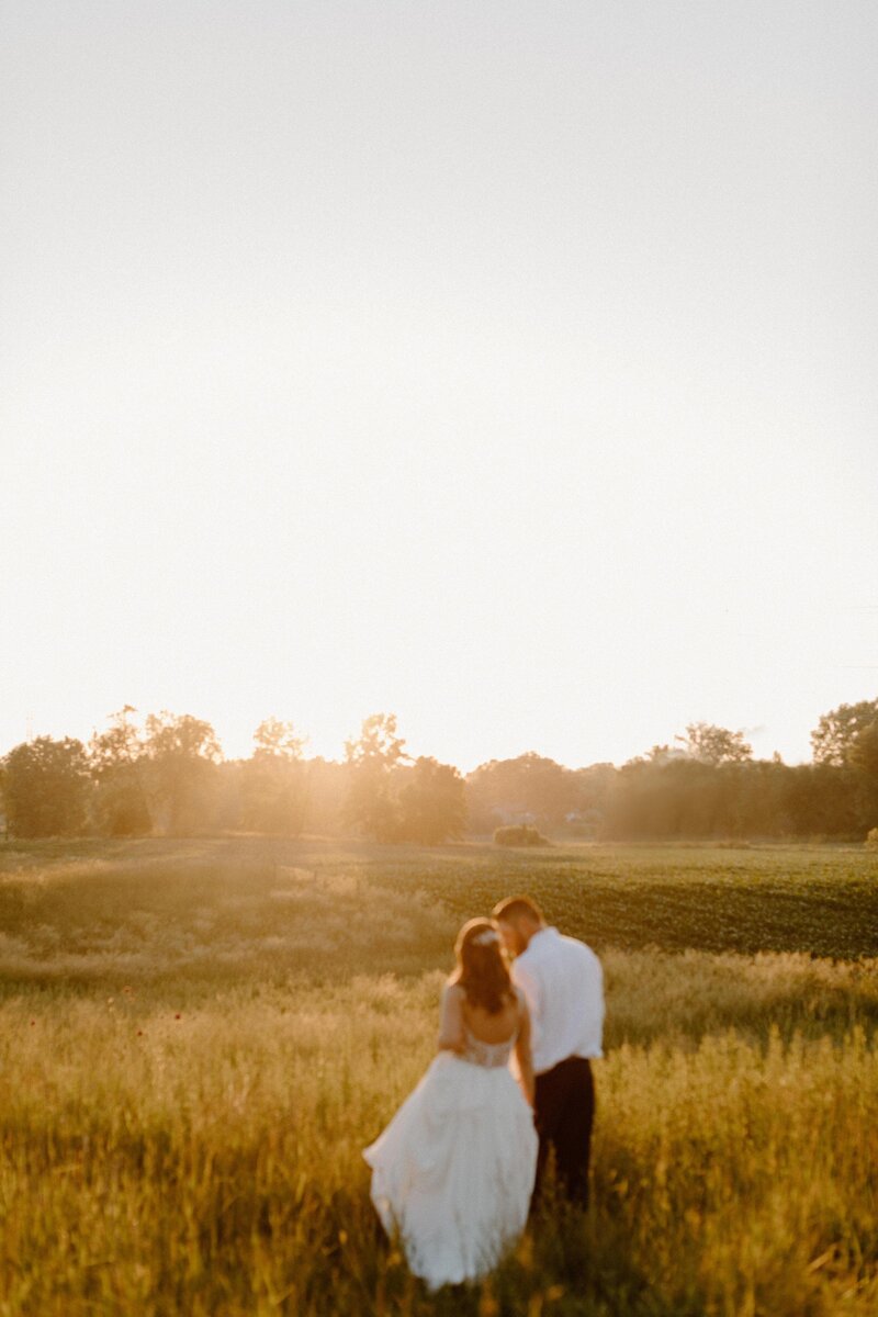 A wedding couple holding hands and walking in a field at sunset 