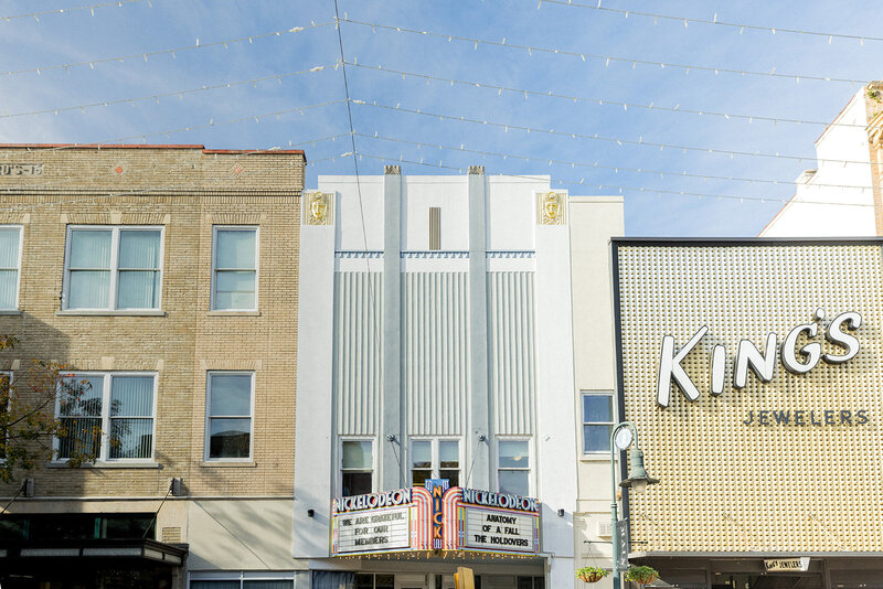 The historic Nickelodeon Theatre in Columbia, SC, with its Art Deco facade and classic marquee sign, nestled between brick buildings on Main Street. String lights hang above, adding charm to the vibrant downtown scene. King’s Jewelers, a local business, stands beside it with a bold modern storefront. Small business branding photography in Columbia, SC, highlighting local culture, historic architecture, and community landmarks.