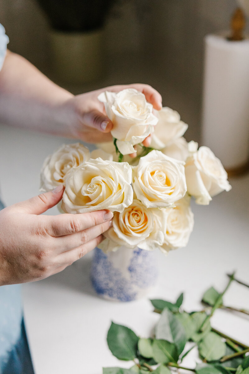 Hands arranging white roses in a blue vase