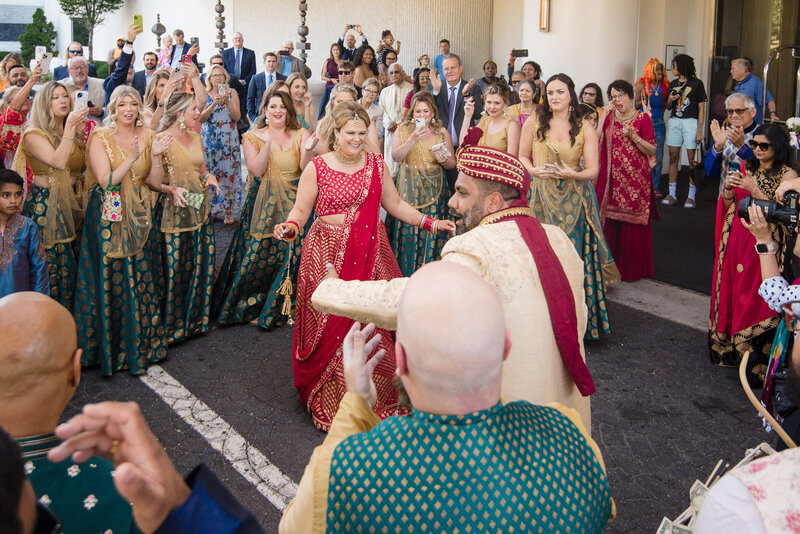 Vibrant Indian wedding baraat celebration at Le Méridien Charlotte. The bride and guests in colorful lehengas and sarees dance joyfully with the groom’s family during the outdoor procession. Captured by a Charlotte Indian wedding photographer specializing in candid, cultural wedding moments full of tradition and energy.