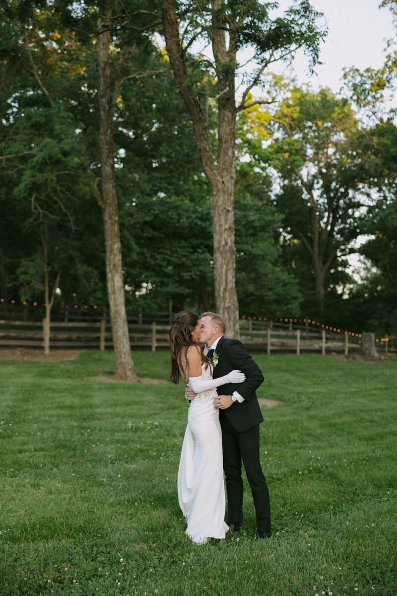 A bride and groom embrace on a porch, sharing an intimate moment. The bride holds a bouquet of white roses, and her veil gently drapes around them.