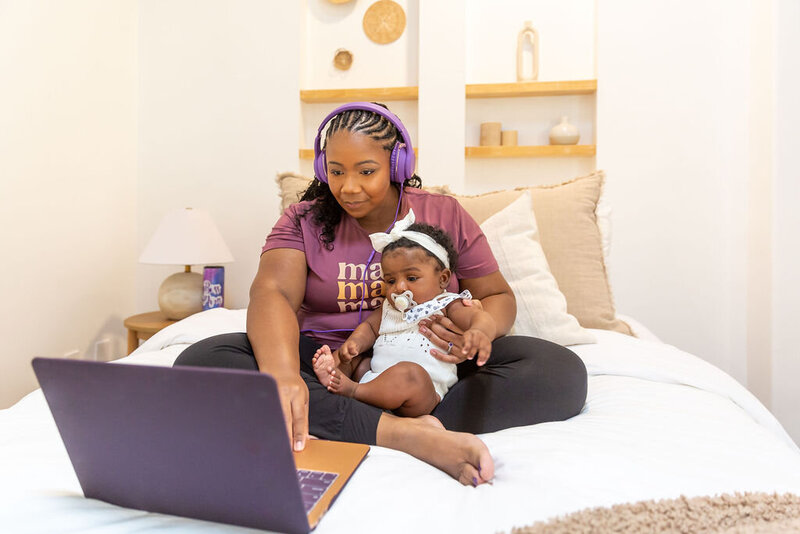 Woman holding baby and working on laptop.